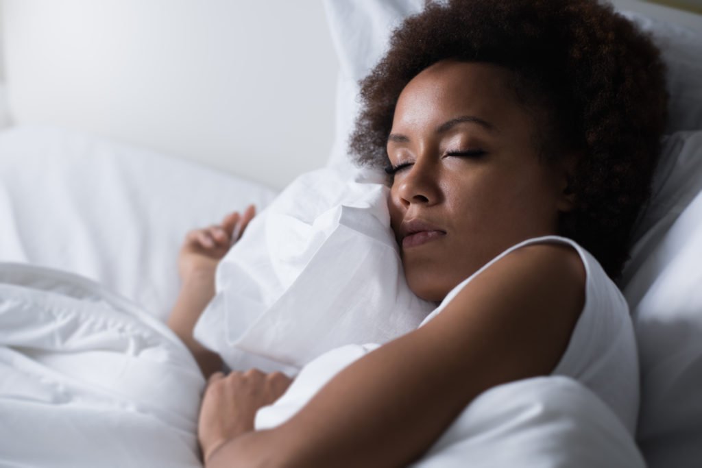 A woman sleeping in white sheets.