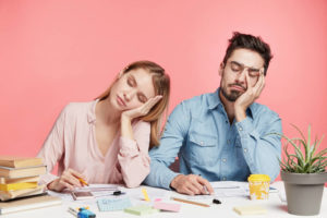 Portrait tired crew of office workers sit at table, fall asleep after working long hours on preparing startup project, feel tiredness, isolated over pink background. People and narcolepsy concept