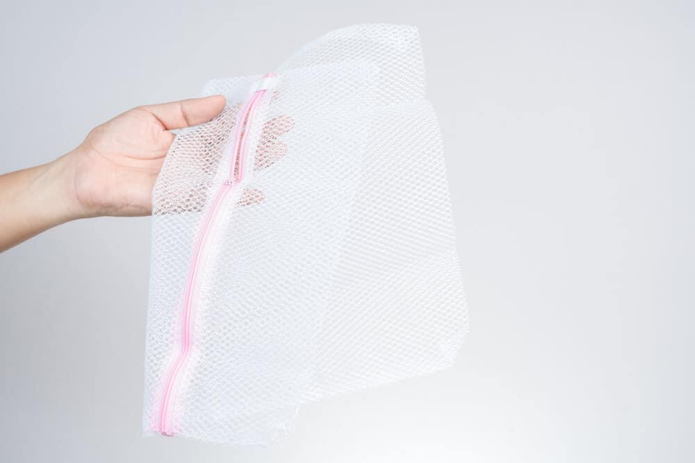 A hand holds a mesh laundry bag against a gray background.