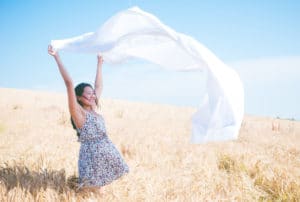 A woman holds a sheet above her head in a field on a sunny day.