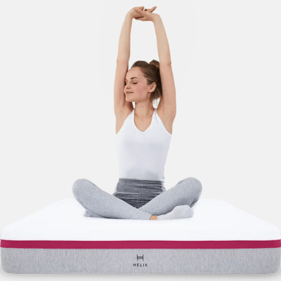 A woman sits cross-legged on a Helix mattress with her arms up.
